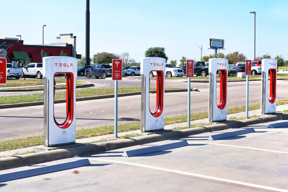 White and red Tesla EV chargers in an open-air parking lot in Corsicana, Texas with Dairy Queen restaurant in background